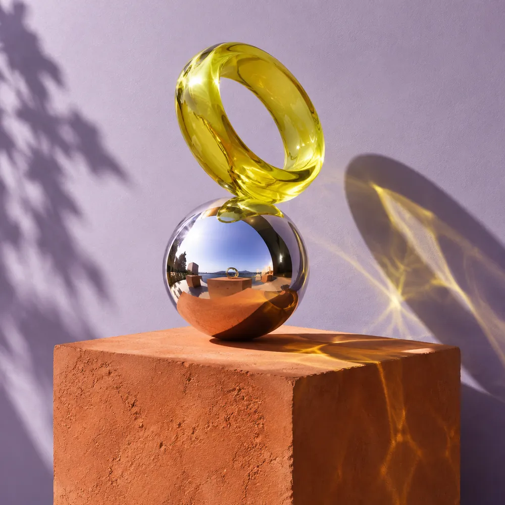 A chrome ball balanced under a yellow glass ring
